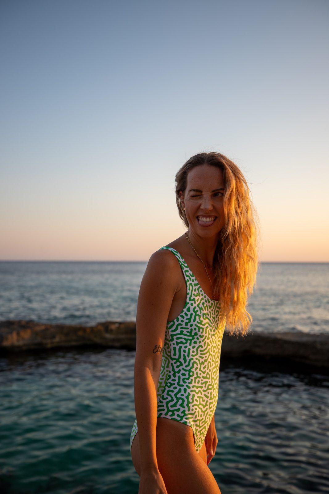 Woman in a green-patterned swimsuit by the sea at golden hour