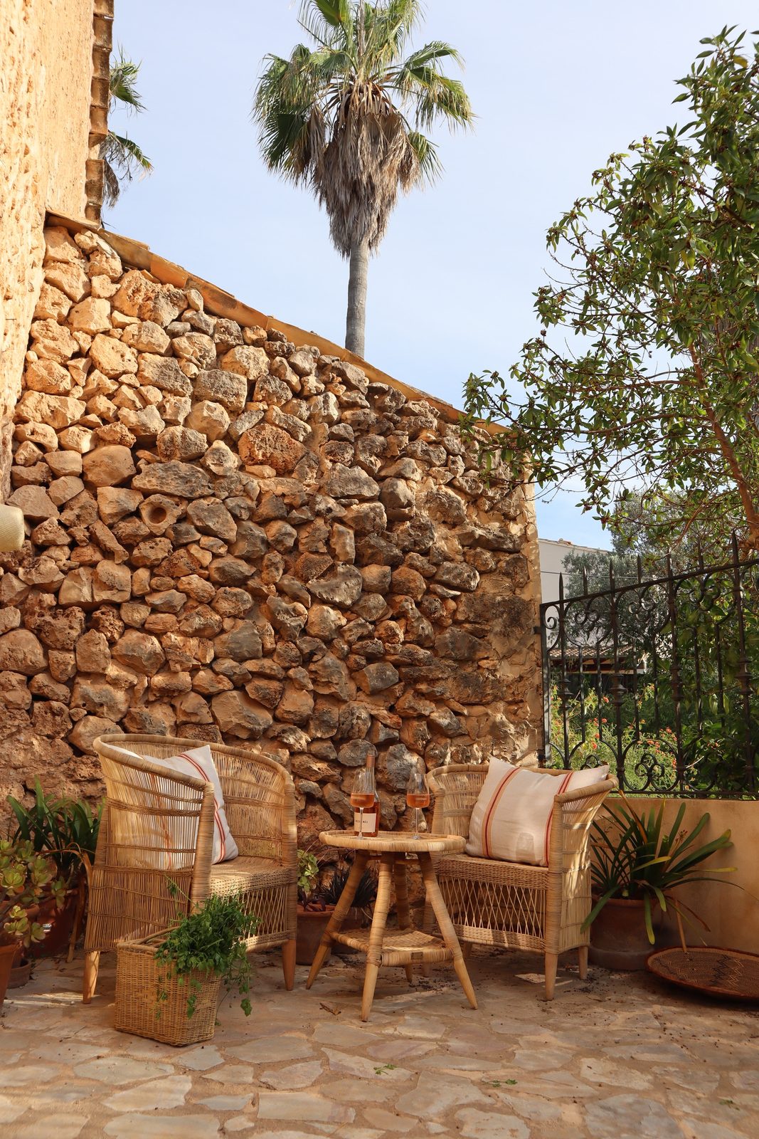 Rustic stone courtyard with a palm, cane chairs and a small wooden table