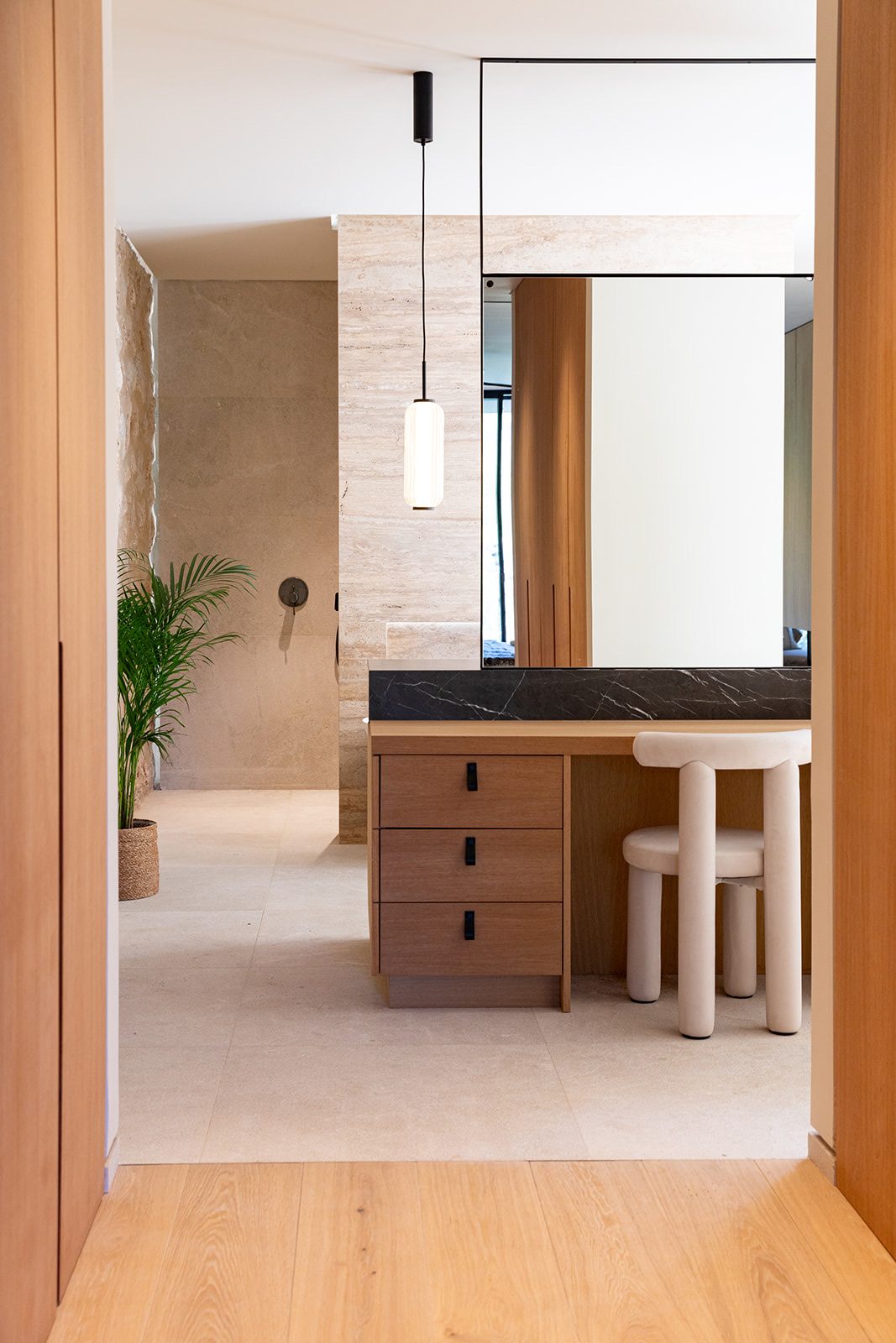 Luxury dressing area in travertine and oak with a black marble vanity and sculptural stool