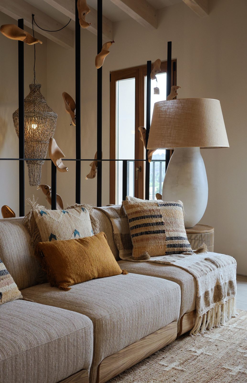 Rustic-luxe living room with a linen sofa, woven pendant lamp and carved wooden bird mobiles